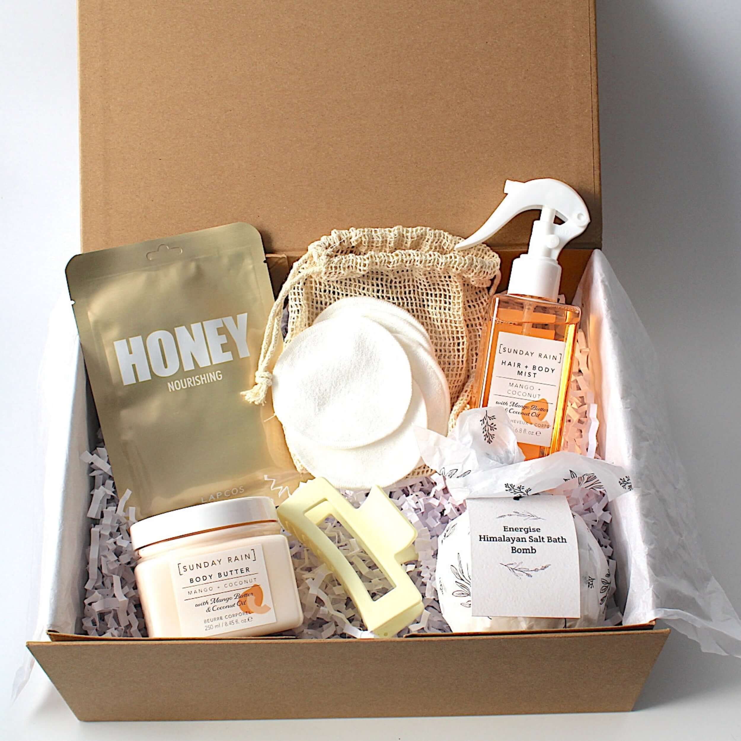 Luxury self-care gift box for ultimate relaxation and pampering. Includes a magnetic keepsake box, hydrating honey sheet mask, Sunday Rain mango & coconut hair and body mist spray, nourishing mango & coconut body butter, Energise Himalayan bath bomb, reusable face cloths in a bamboo bag, and a stylish claw hair clip. Perfect for birthdays, self-care gifts, and spa gift sets.