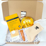 Golden Christmas pamper gift box with hyaluronic acid face mask, gold eye patches, citrus bath bar, caramel lip balm, cream bow socks and hot chocolate