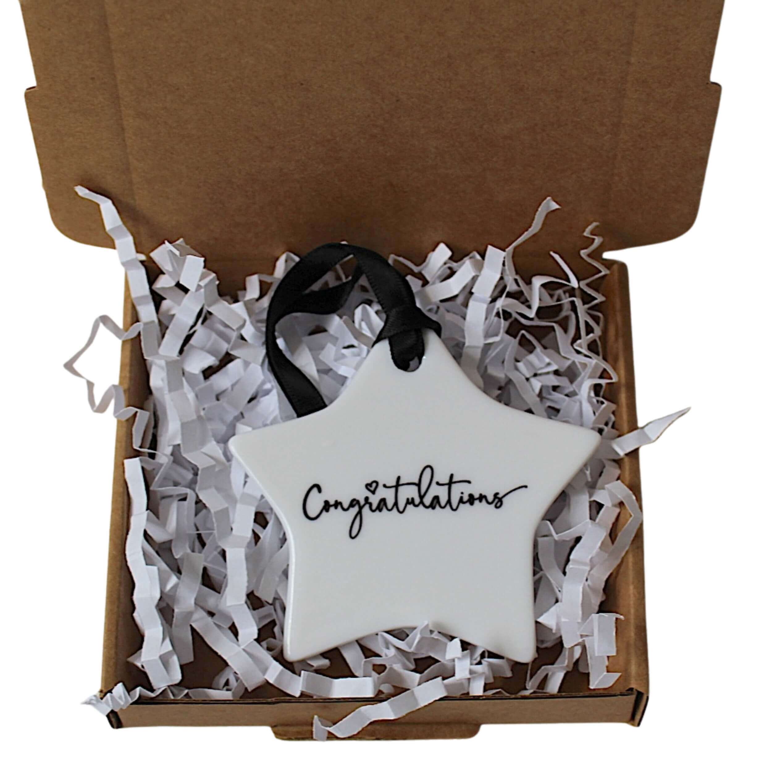 A white star-shaped ceramic ornament with 'Congratulations' written in black script, presented inside an open brown gift box filled with white crinkle paper.