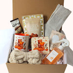 Magnetic closure gift box with mug wth orange handle bear sitting on pumpkin reading, matching coaster, cookie and fudge clusters, wool socks in grey, aromatherapy bath salts, sunday rain mango body mist, grey bow spa head band, galaxy hot chocolate sachet. 