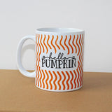white mug white orange wavy lines, black writing 'hello pumpkin' on side table with white background. 