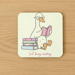 Goose coaster featuring a cute goose reading a book with text 'Just busy reading' on a wooden surface.