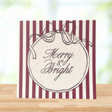 A square greeting card with burgundy and cream vertical stripes, featuring a central cream oval with a ribbon illustration and the words 'Merry & Bright' in script, displayed on a wooden surface with a blurred light background.