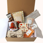 An autumn-themed gift box filled with cosy items including a beige bow headband, a white mug with a pumpkin book illustration, Galaxy chocolate hot chocolate, 'HeAutumn' coaster, cookie and fudge clusters, aromatherapy bath salts, luxury socks and mango and coconut spray , all arranged in a magnetic closure box.