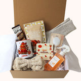 An autumn-themed gift box filled with cosy items including a beige bow headband, a white mug with a pumpkin book illustration, Galaxy chocolate hot chocolate, 'HeAutumn' coaster, cookie and fudge clusters, aromatherapy bath salts, luxury socks and mango and coconut spray , all arranged in a magnetic closure box.