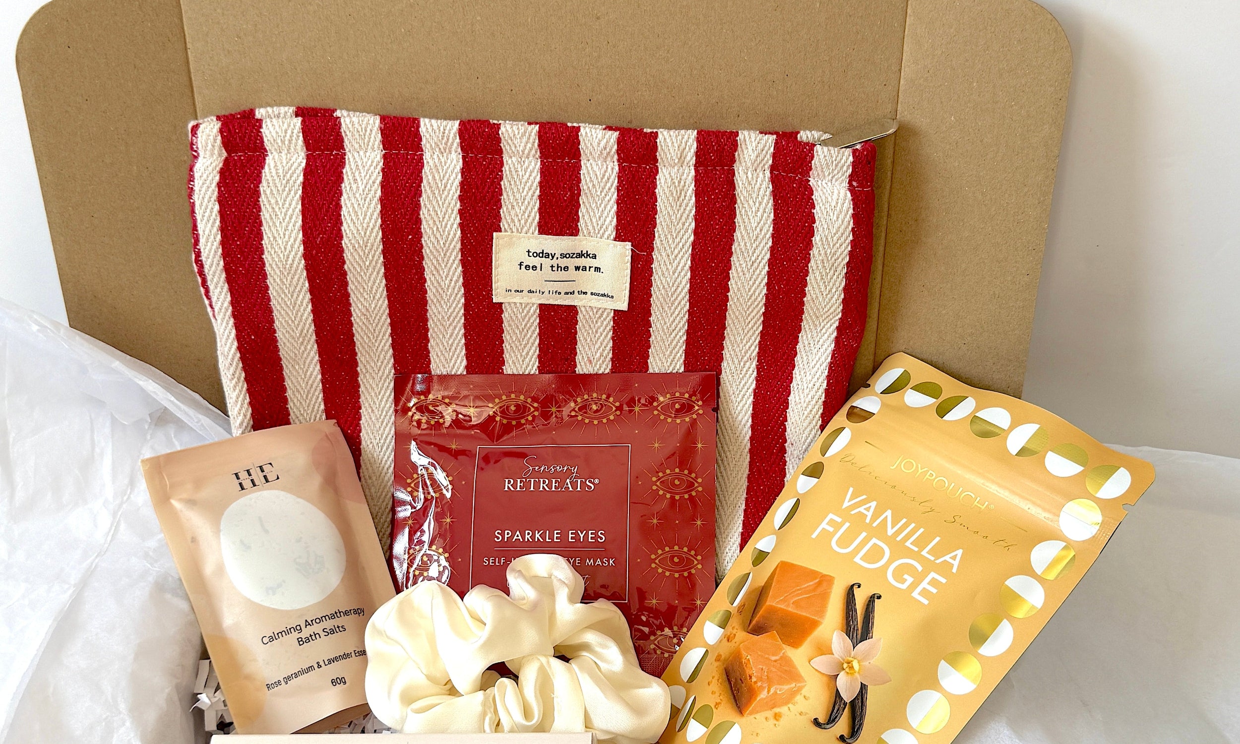 Red striped wash bag, aromatherapy bath salts, sensory retreat sparkle eyes self heated eye mask, vanilla fudge, hair scrunchy and 3 aromatherapy scented candles  