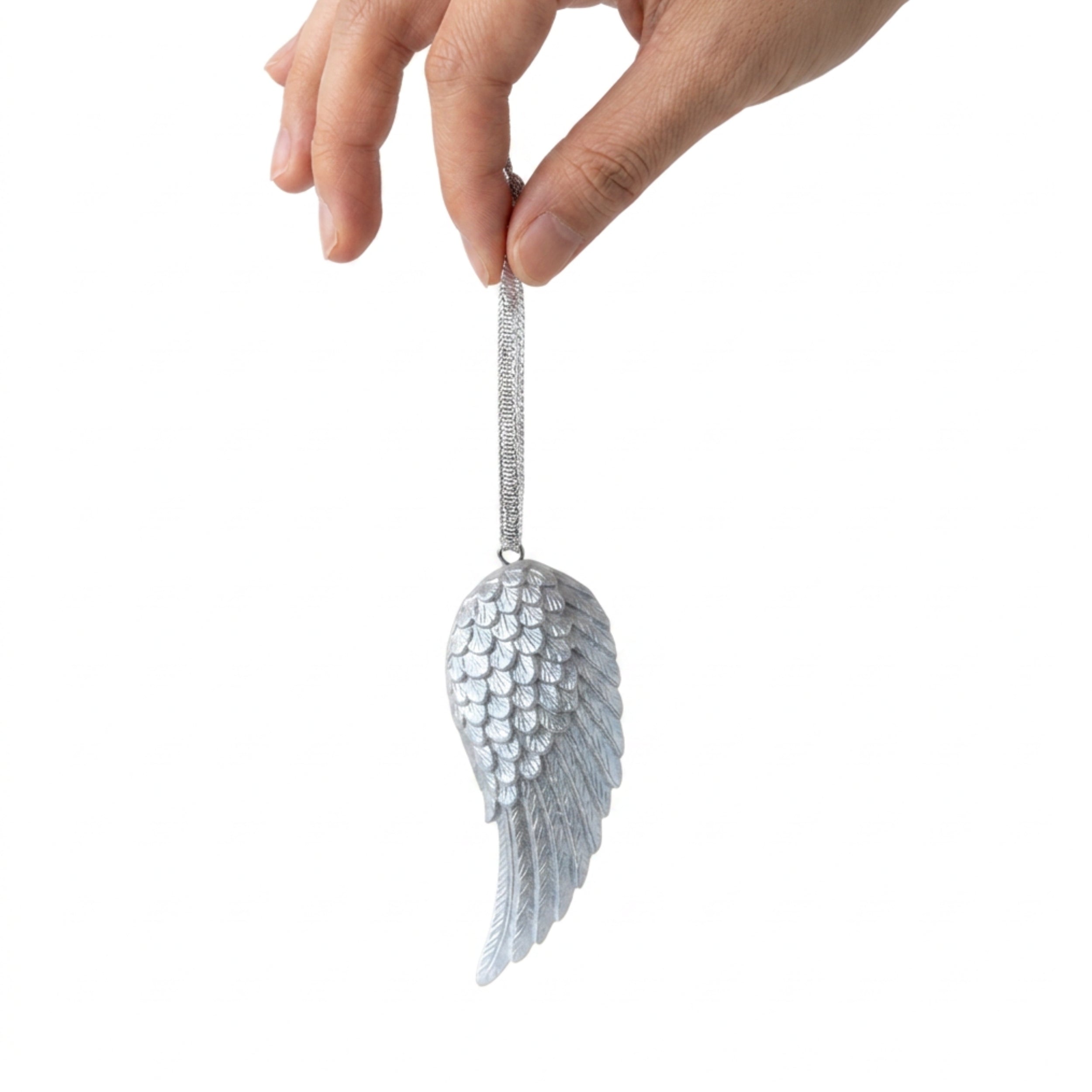 A hand holding a silver angel wing ornament against a plain white background.