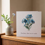 A square greeting card with a watercolor illustration of blue forget-me-nots and the printed phrase 'Sometimes there are no words.