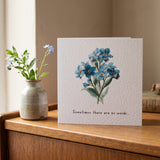 A square greeting card with a watercolor illustration of blue forget-me-nots and the printed phrase 'Sometimes there are no words.