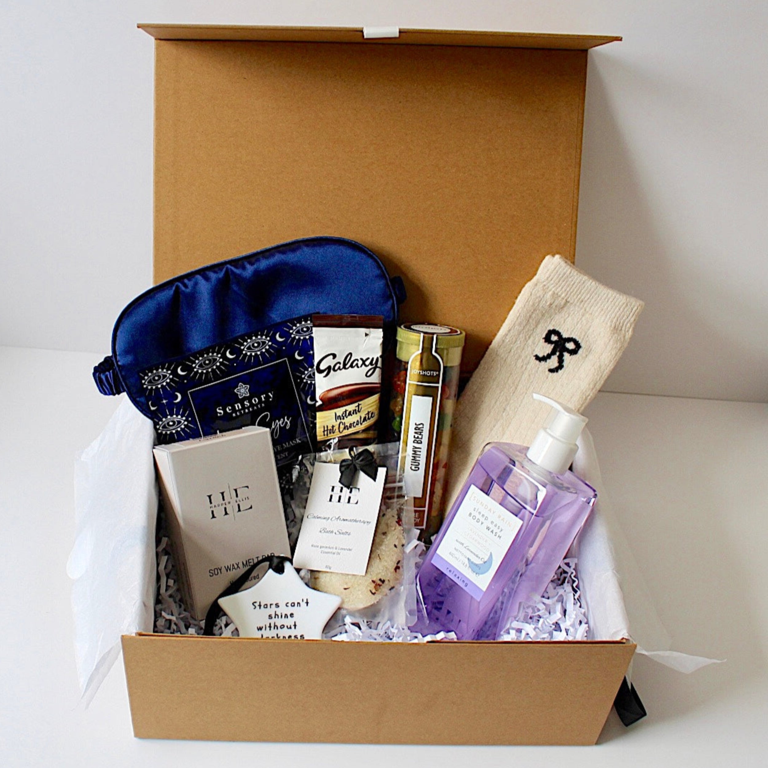 Stars Pamper box in magnetic closure box,  satin sleep mask, galaxy hot chocolate, calming bath salts, ceramic keepsake, gummy bears jelly sweets, soy wax melts, cosy socks and sunday rain sleep easy  body wash. 
