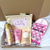 A curated gift box set containing a beige canvas pouch with a pink label reading 'You look beautiful today', raspberry body butter, 60g aromatherapy bath salts, berries bubble tea sheet mask, and a tube of strawberry bom boms,  all arranged in white crinkle paper inside a brown cardboard box. 