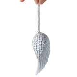 A hand holding a silver angel wing ornament against a plain white background.