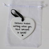 A white ceramic heart-shaped ornament with black printed text reading 'Distance means nothing when you have someone so special!' and a small black heart at the bottom, hanging from a black ribbon. It is displayed inside a clear white drawstring pouch on a light background.