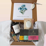An open brown gift box filled with white tissue paper and shredded paper filler, containing a card with blue flowers and the text 'Sometimes there are no words.