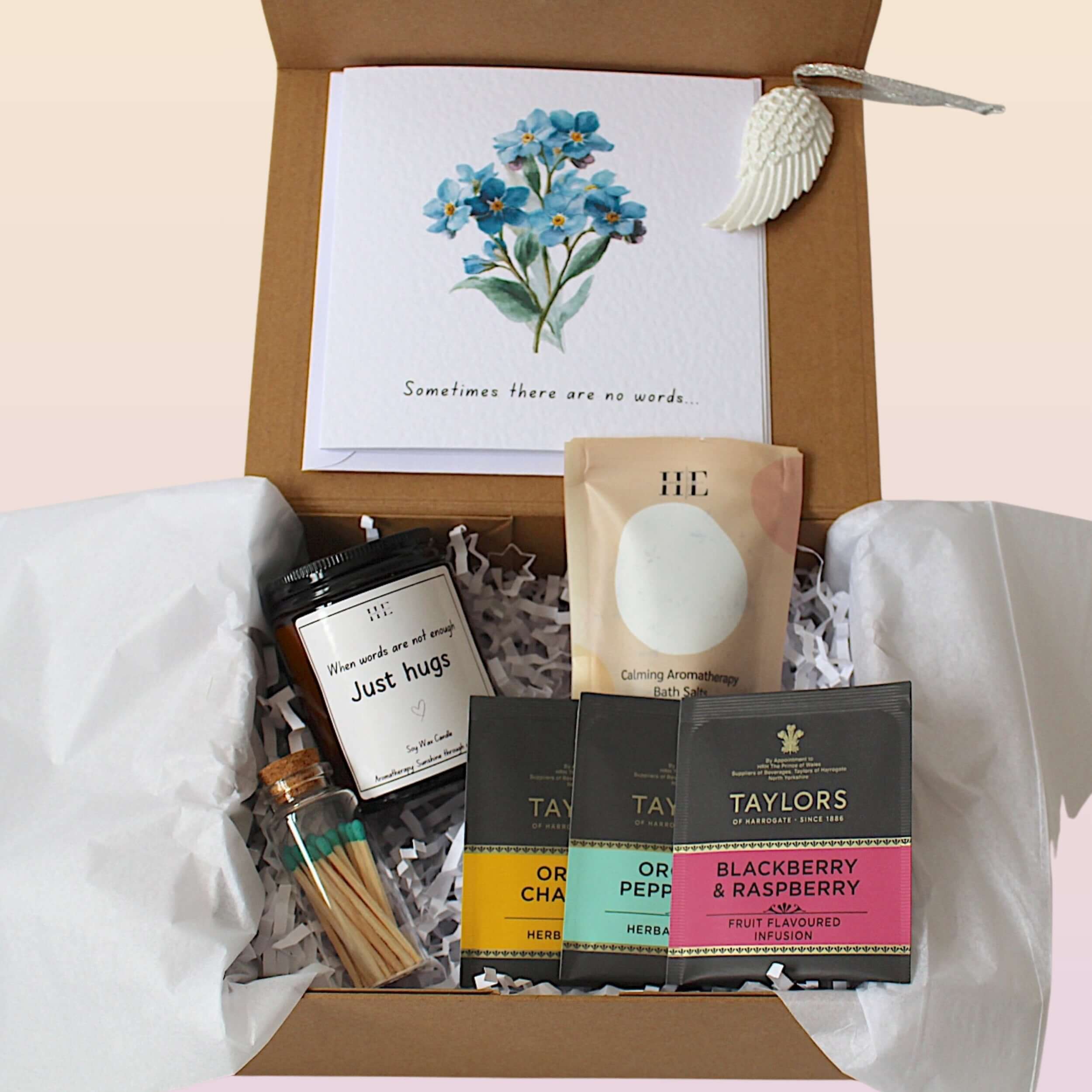 An open brown gift box filled with white tissue paper and shredded paper filler, containing a card with blue flowers and the text 'Sometimes there are no words.