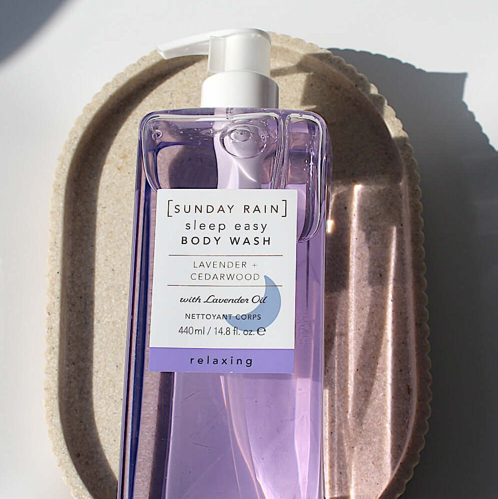Purple bottle of Sunday Rain body wash on a textured beige surface
