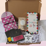 A curated gift box set in an open brown gift box filled with white shredded paper. Visible items include a pink Bubble Tea Sheet Mask from bubble beauty, a box of Joybars Thank You milk chocolate, three Taylors Blackberry & Raspberry tea sachets, and a white star-shaped thank you keepsake